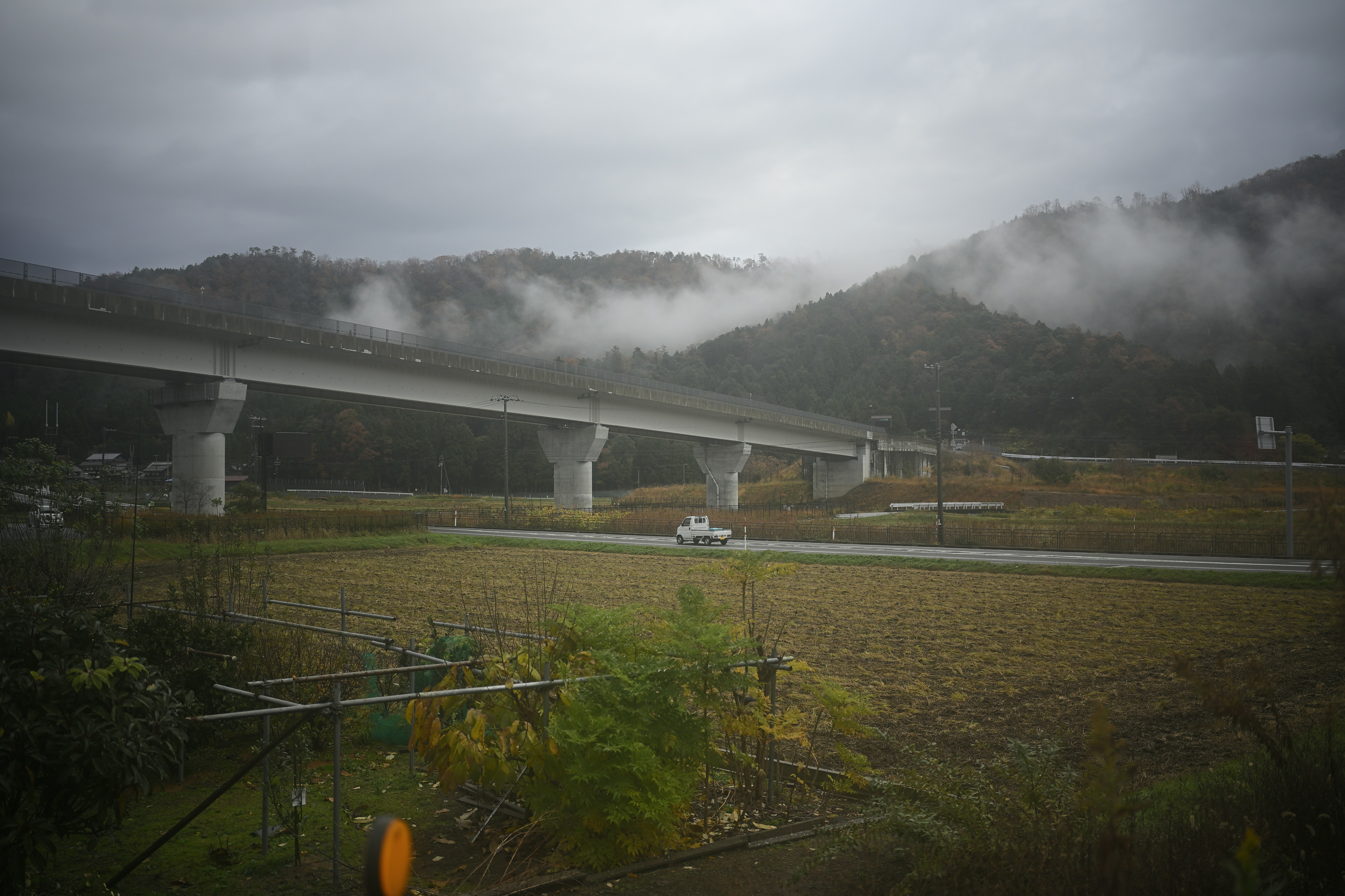 Eine Brücke spannt sich über ein Feld mit Bergen.