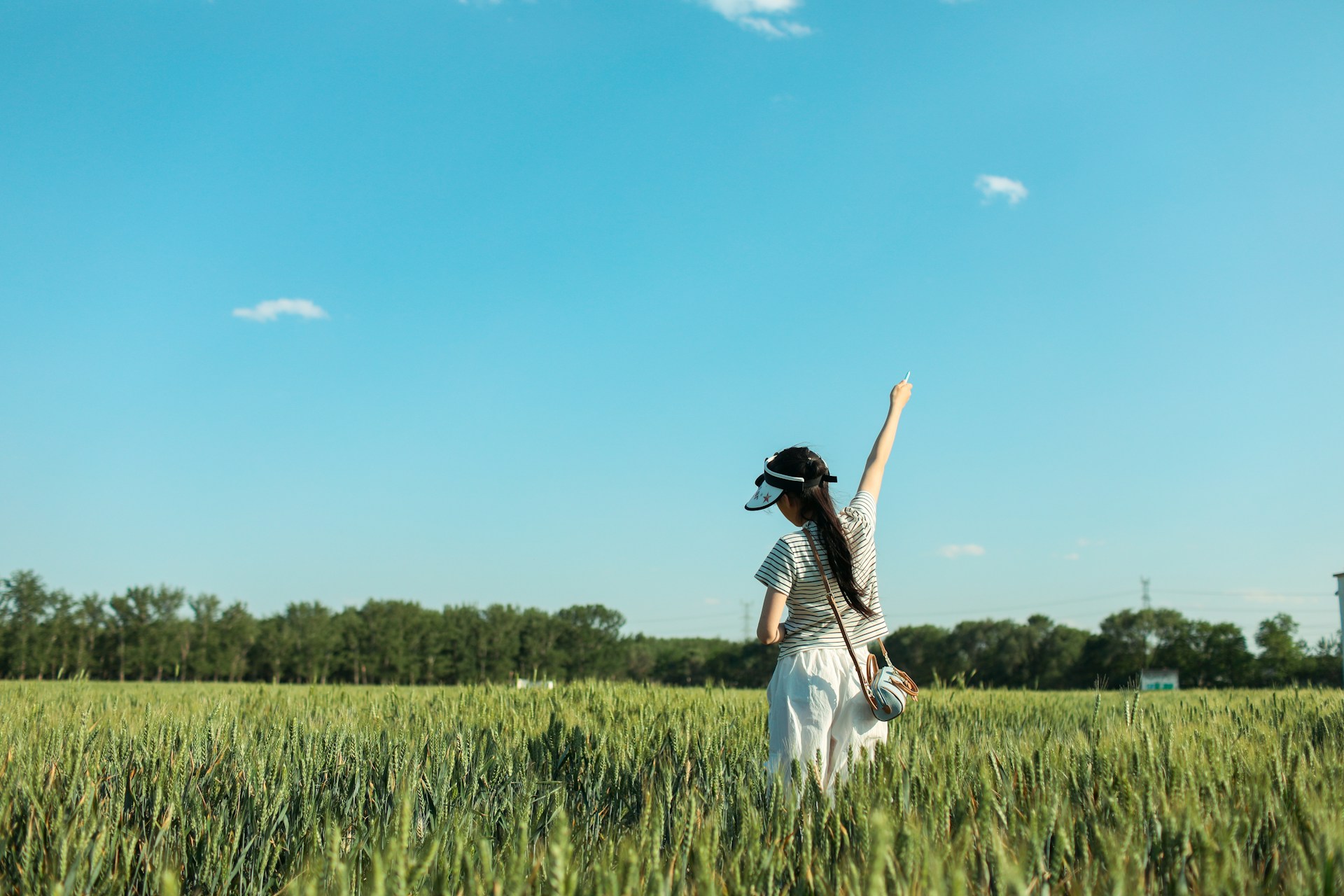 Woman raises arm in a green field under blue sky.