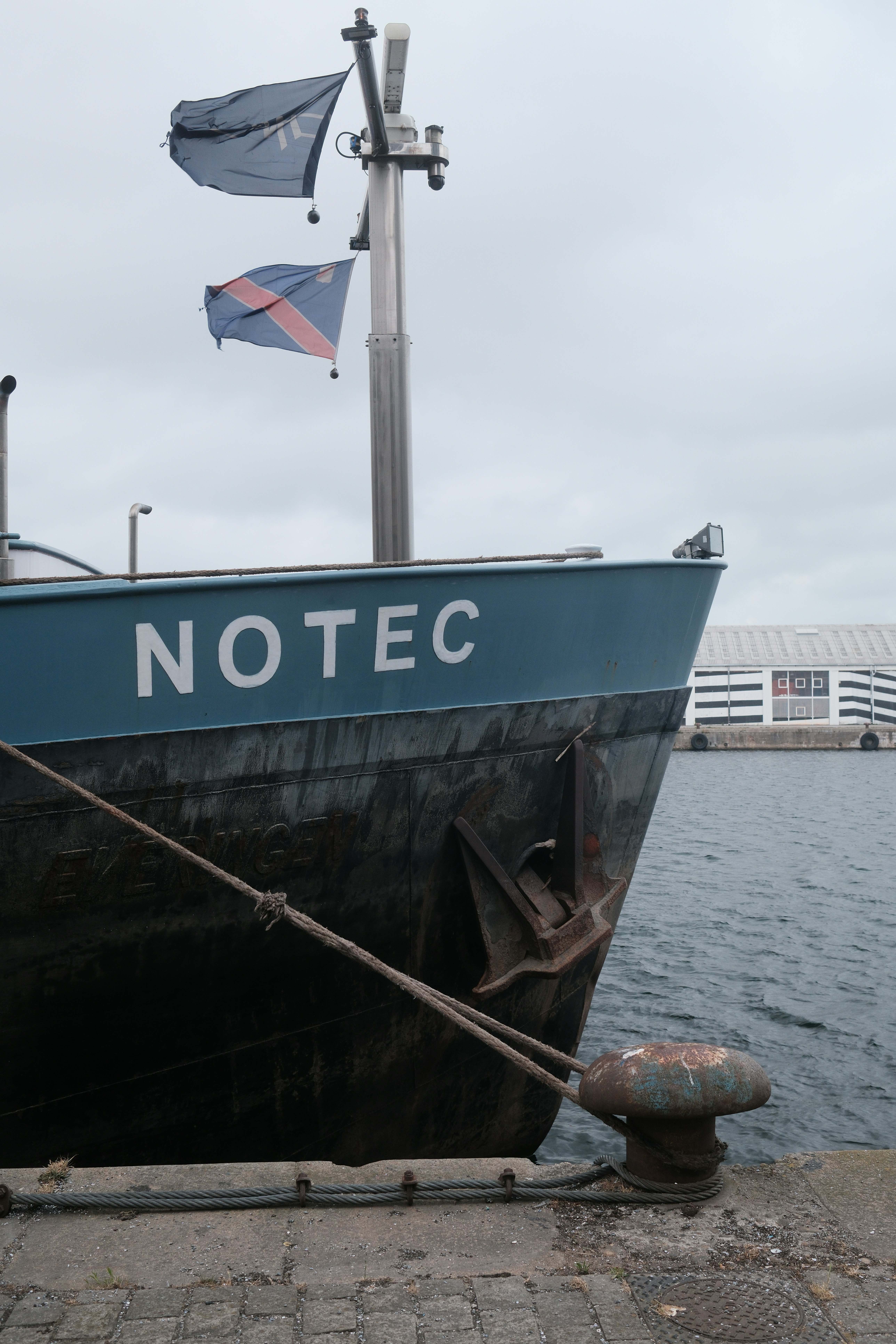 A ship named notec sits dockside with flags.