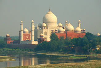 The taj mahal stands near a calm river.