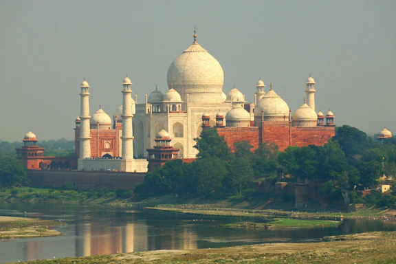 The taj mahal stands near a calm river.
