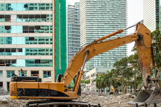 A yellow excavator stands near city buildings.