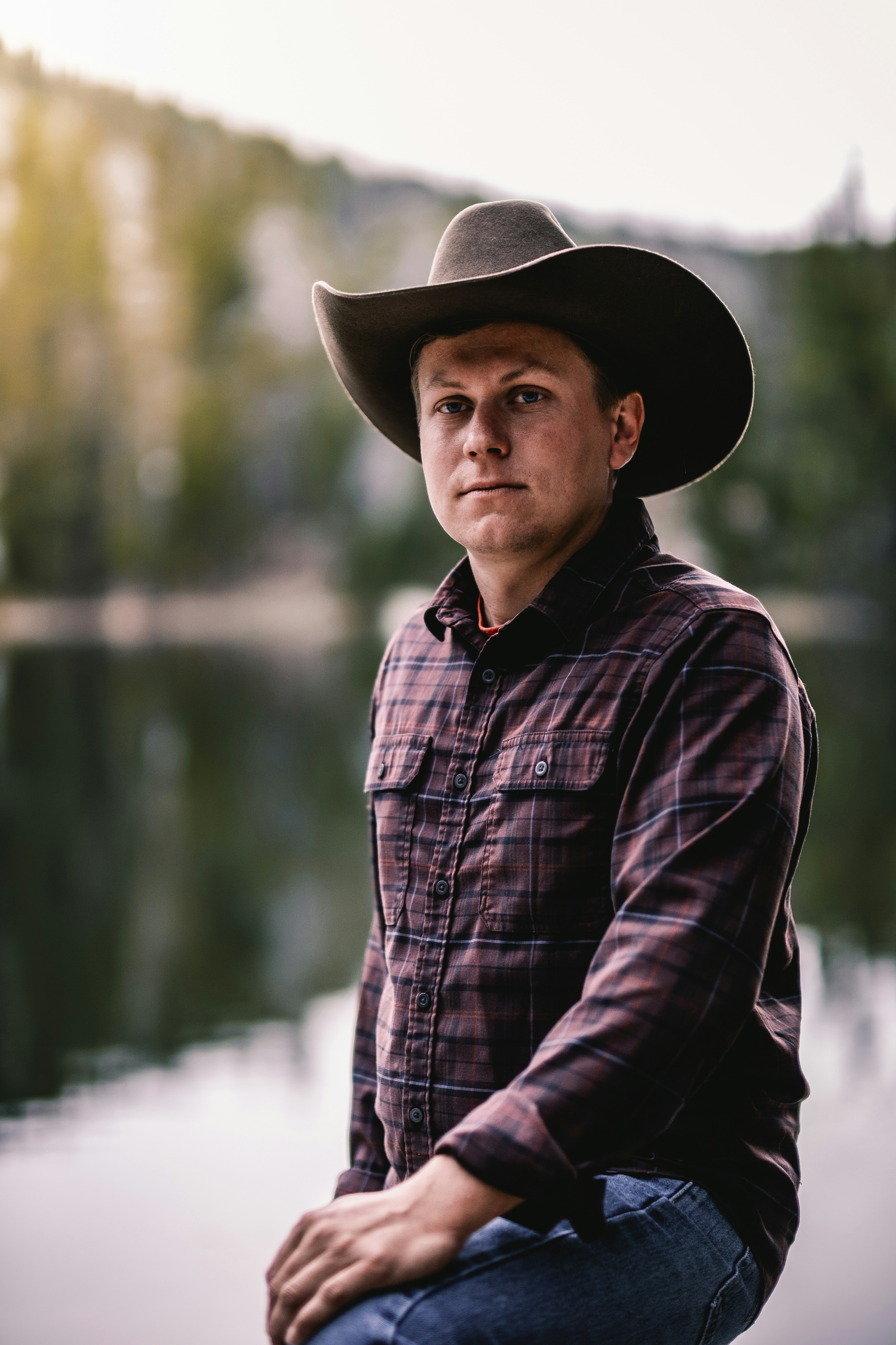 Un cowboy in camicia a quadri posa in riva al lago