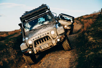 Two jeeps are driving off-road, covered in mud.