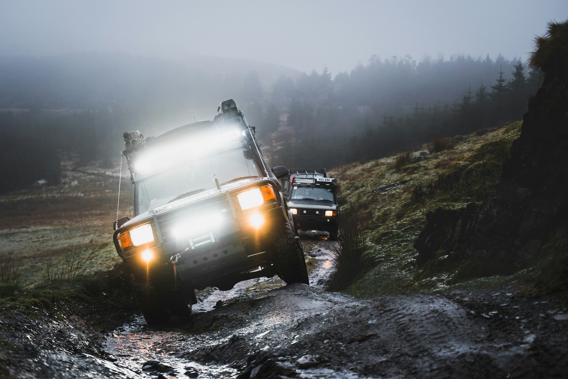 Off-road vehicles navigate a muddy, foggy trail.