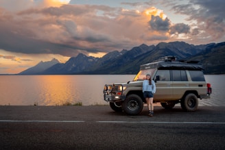 A woman stands by her car, overlooking mountains.