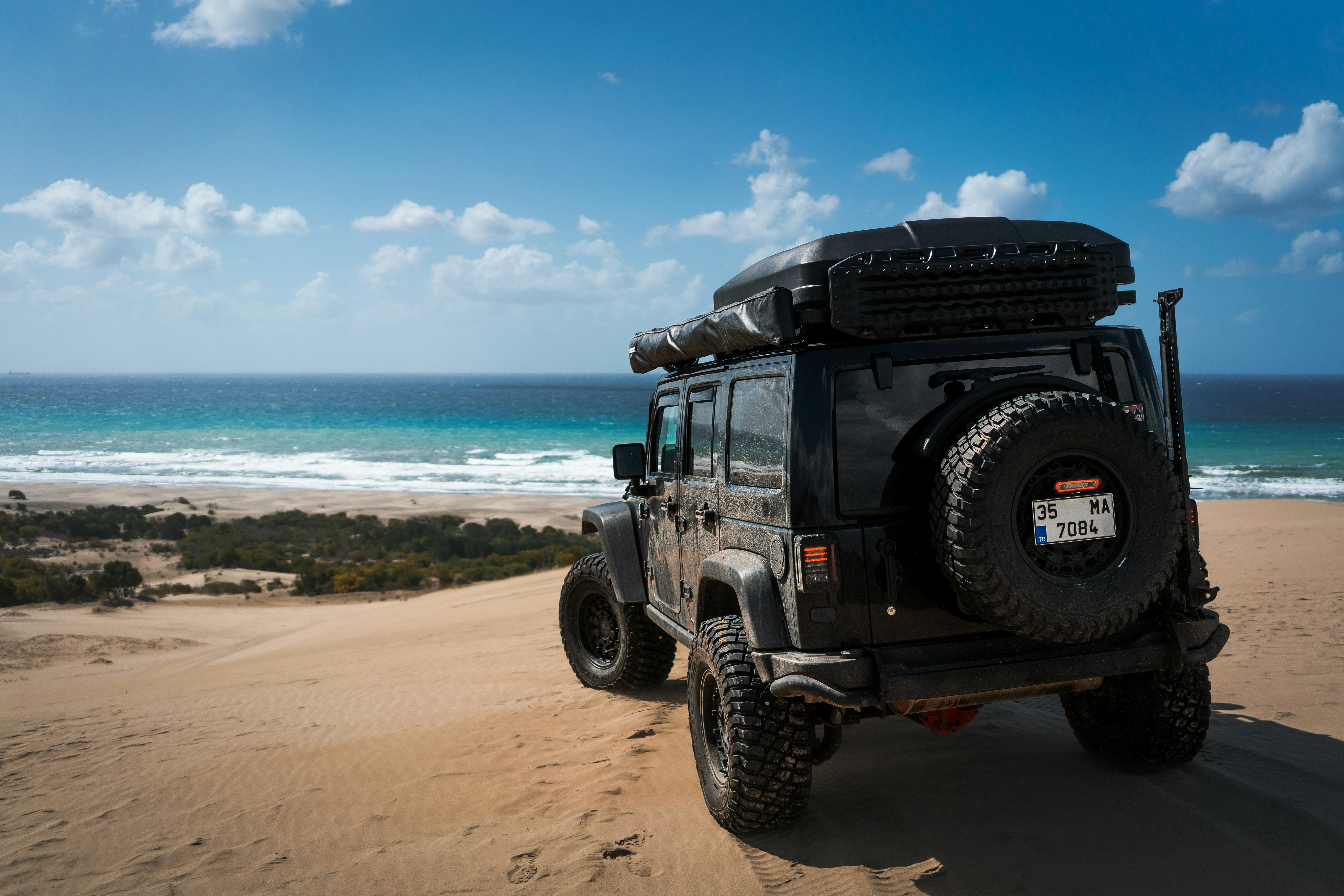 지프차는 모래 언덕에서 바다를 내려다보고 있습니다.