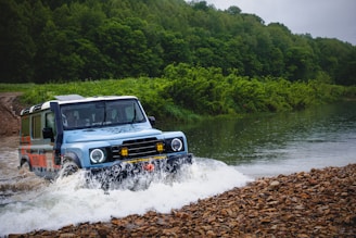 A blue jeep splashes through a river.