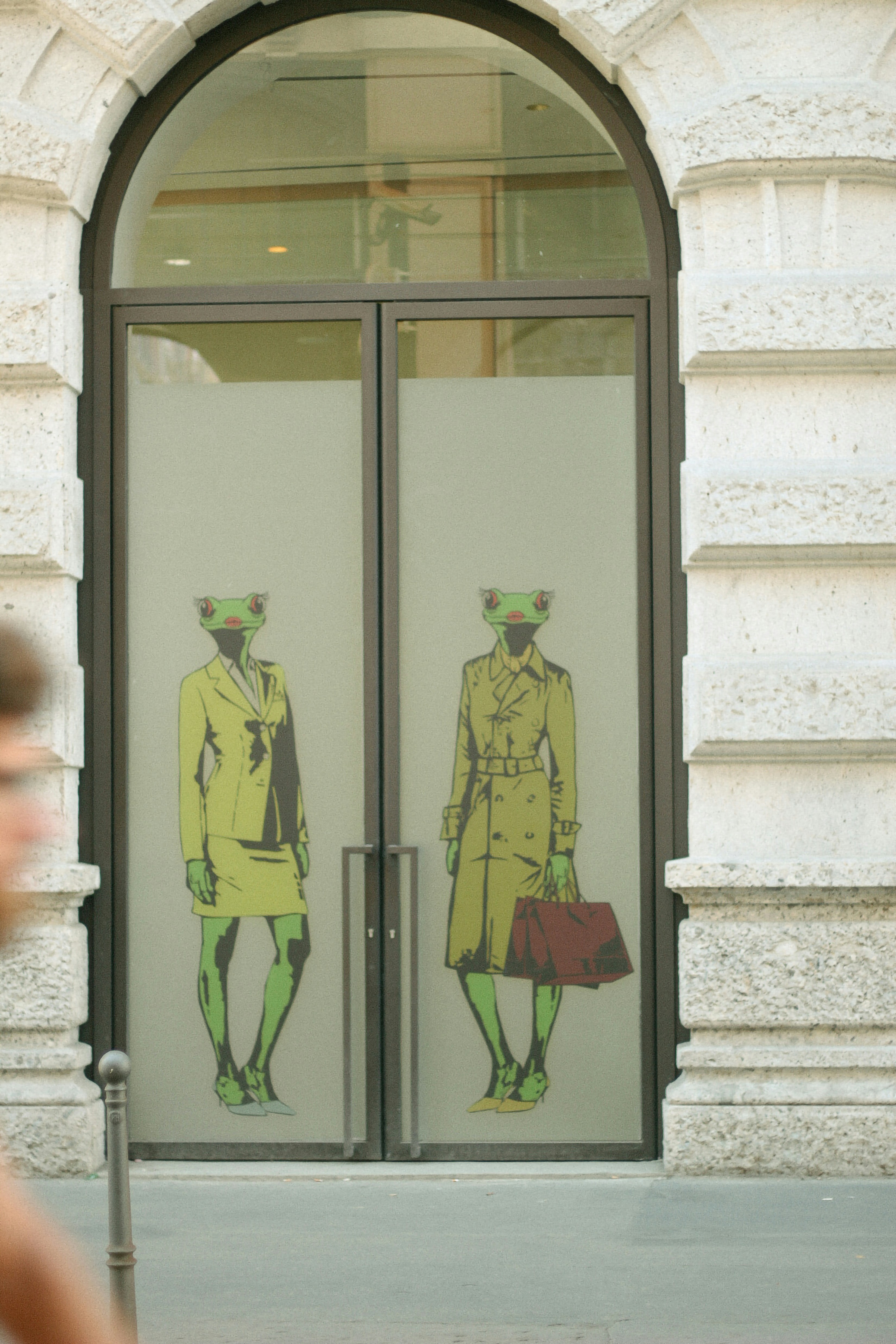 Frog-headed figures adorn a storefront's glass doors.