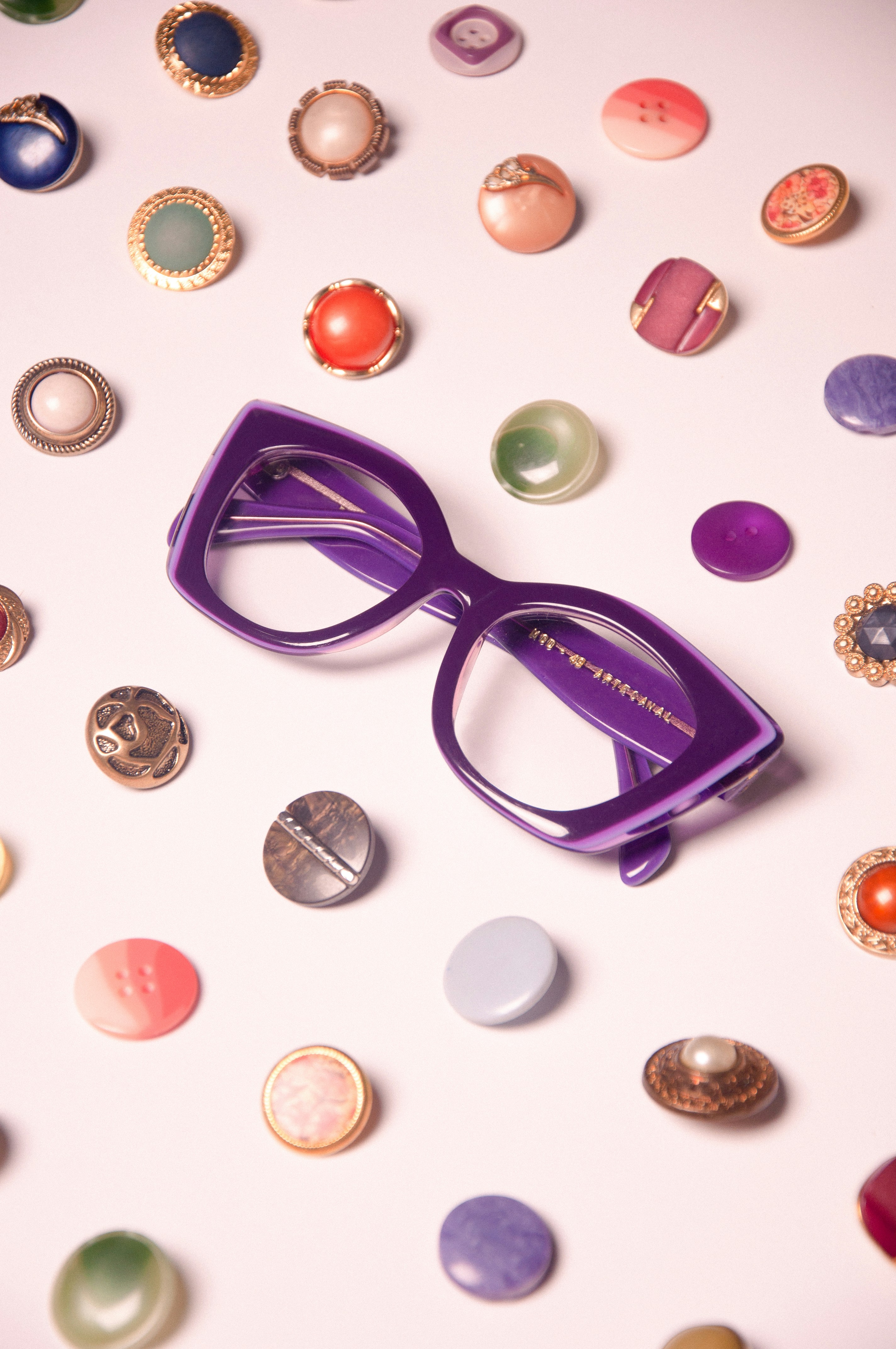 Purple eyeglasses surrounded by colorful buttons.