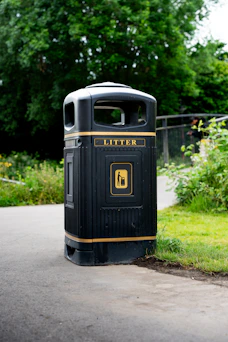 Here's a caption for the image: black litter bin on a path.
