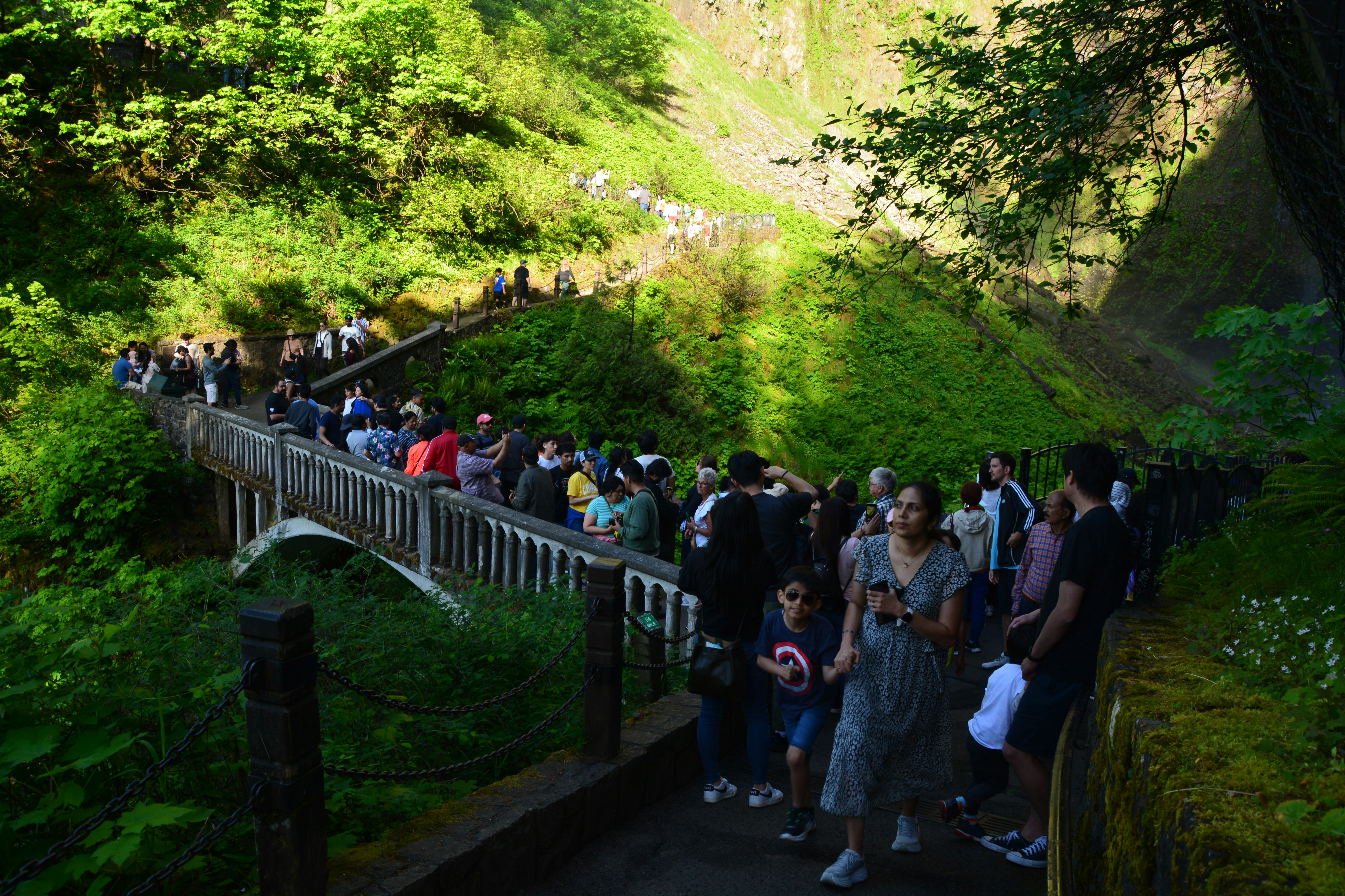 People walk along a trail towards a waterfall.