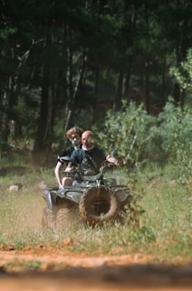 Two people ride an atv through a forest.