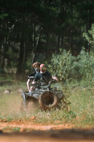 Two people ride an atv through a forest.