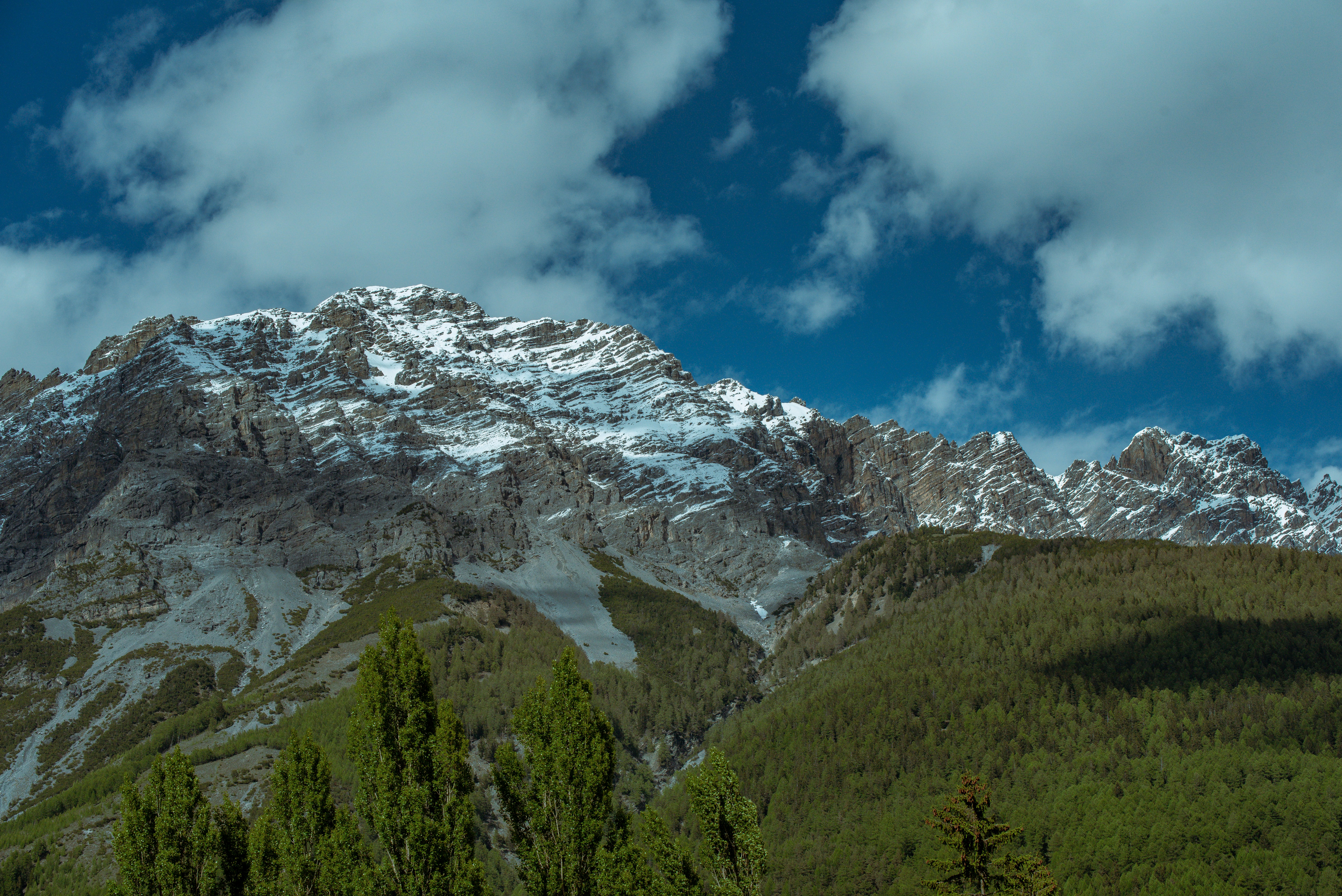 Snowy mountain peaks against a cloudy, blue sky.