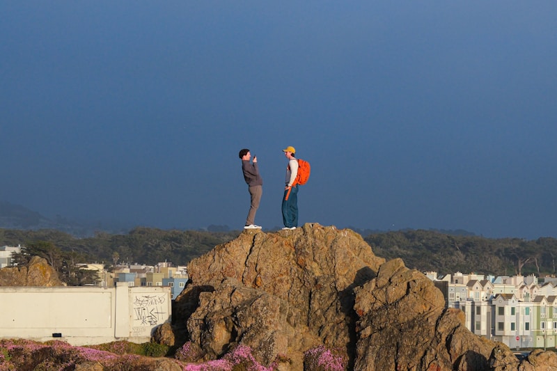Two people stand atop a rock, taking pictures.