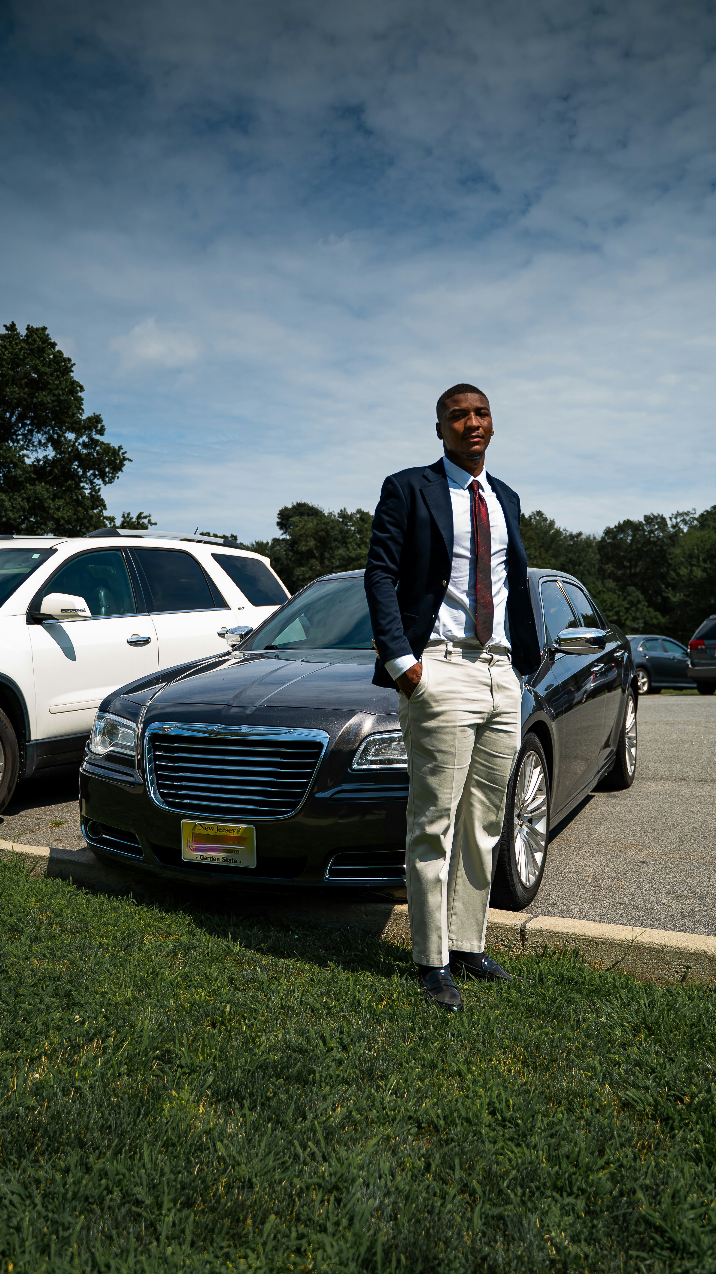A well-dressed man poses near a luxury car