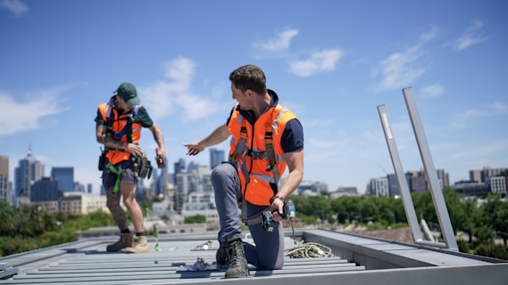 Construction workers wearing safety gear are on a rooftop.
