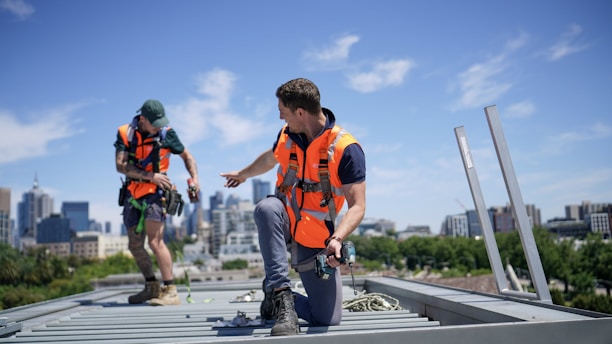 Construction workers wearing safety gear are on a rooftop.