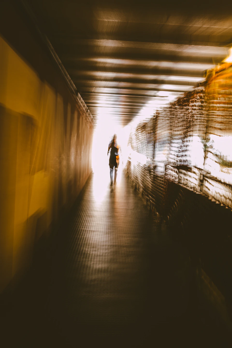 Person walking through underground tunnel with sunlight illuminating their back to right