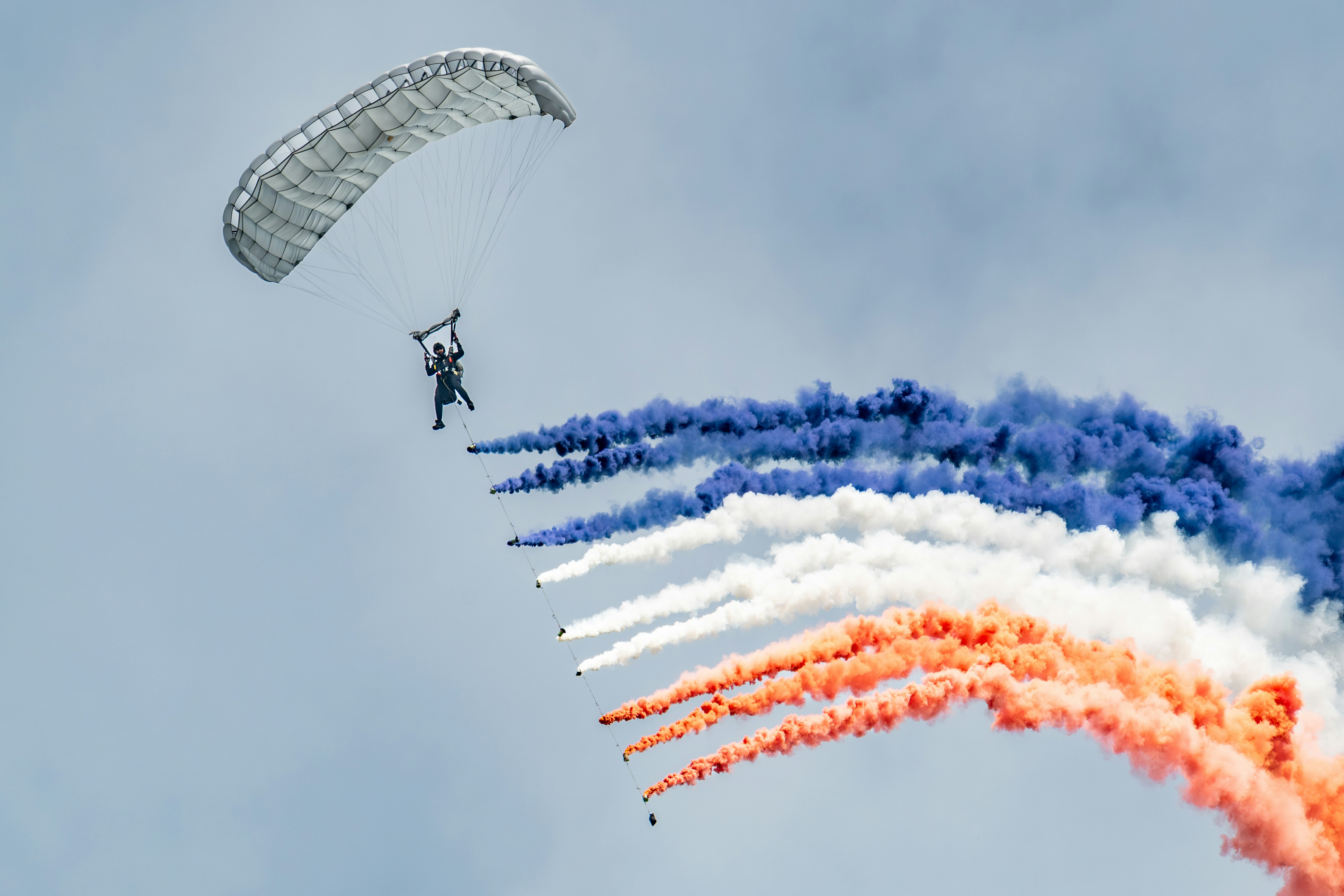Un parachutiste descend avec des traînées de fumée colorées.