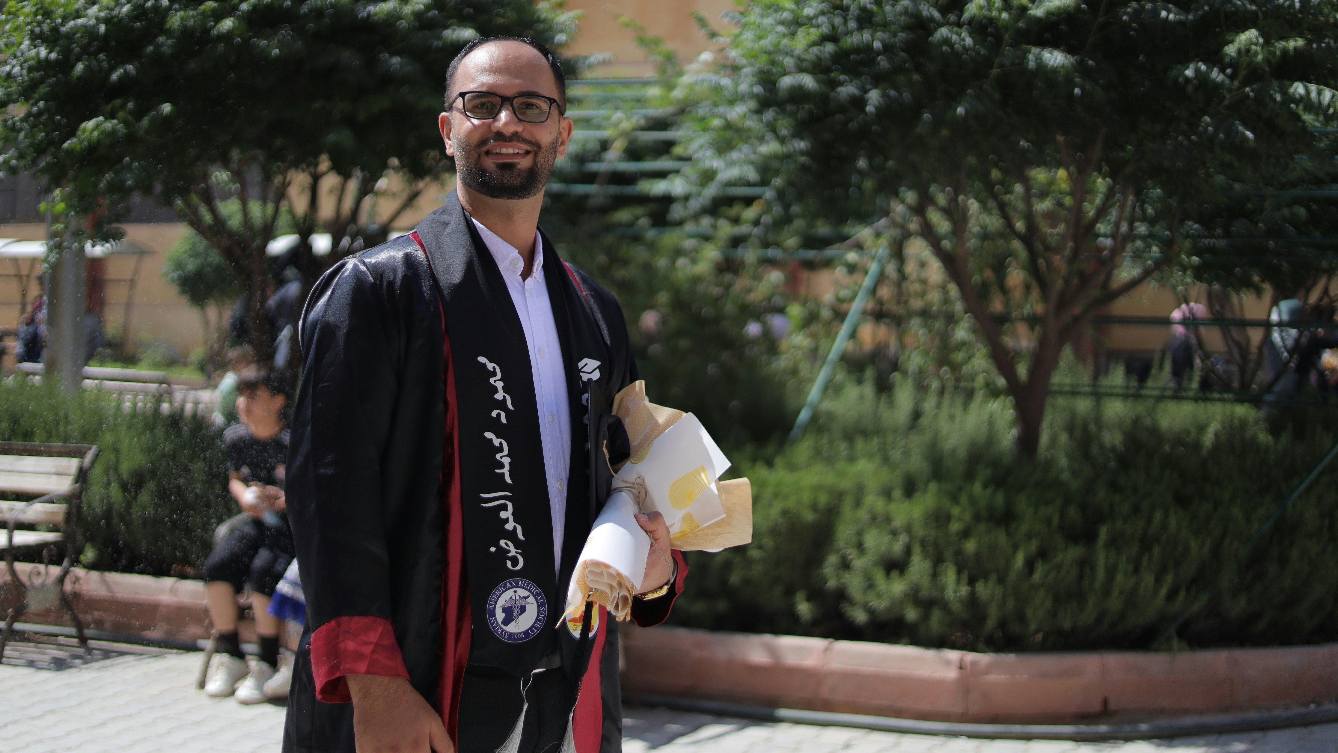 Ein Mann im Abschlusskleid lächelt in die Kamera.