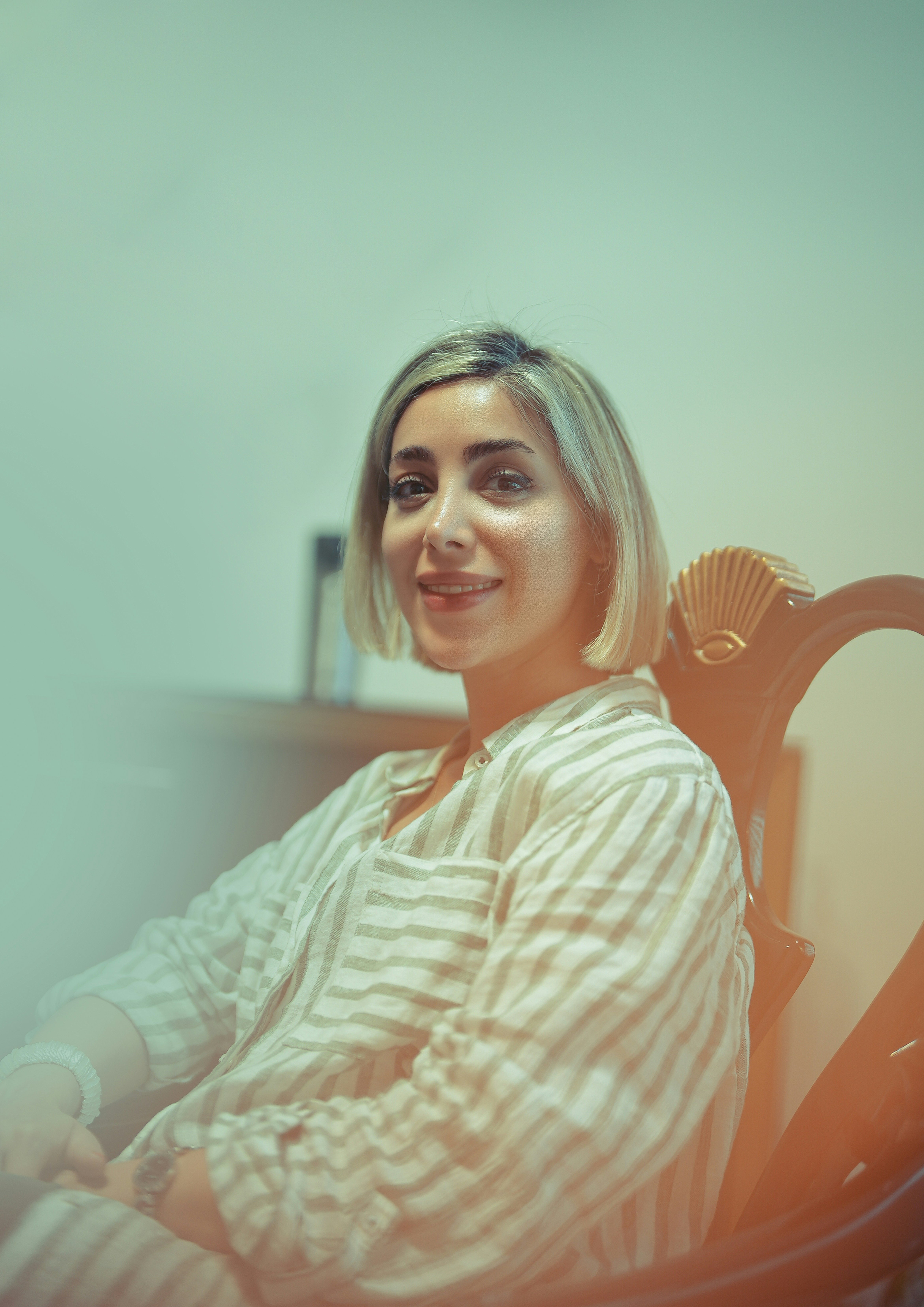 A smiling woman sits comfortably in a chair.