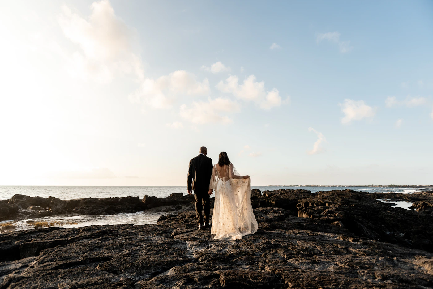 Couple in elopement attire exchanging vows on the deck of a vessel in the Galapagos with the ocean and volcanic island visible behind them
