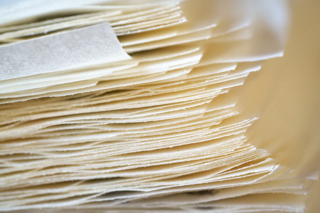 Stapel handgeschöpfter Papierbögen mit Büttenrand in warmem Cremeton, Nahaufnahme