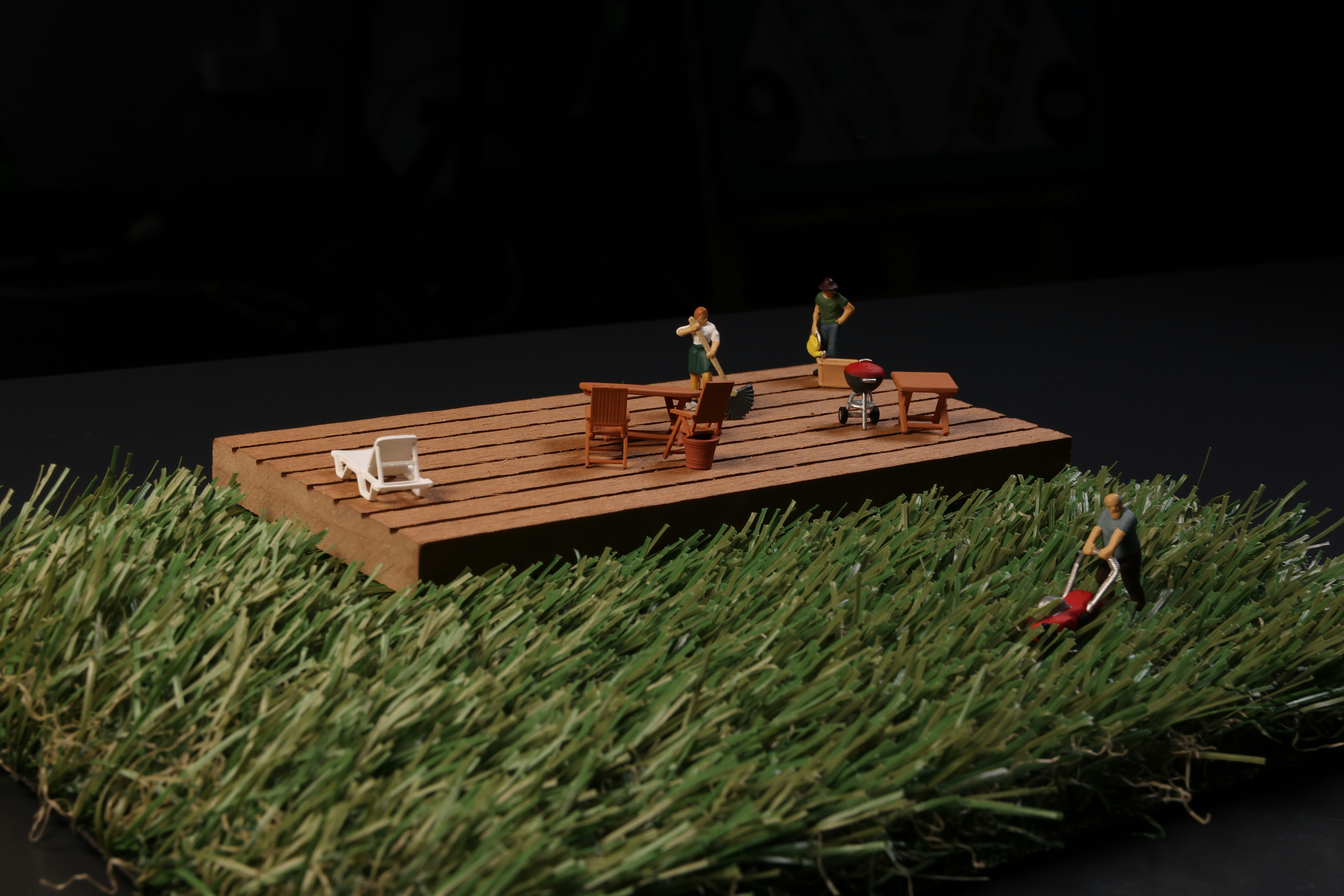 Tiny figures play on a wooden deck on the grass.