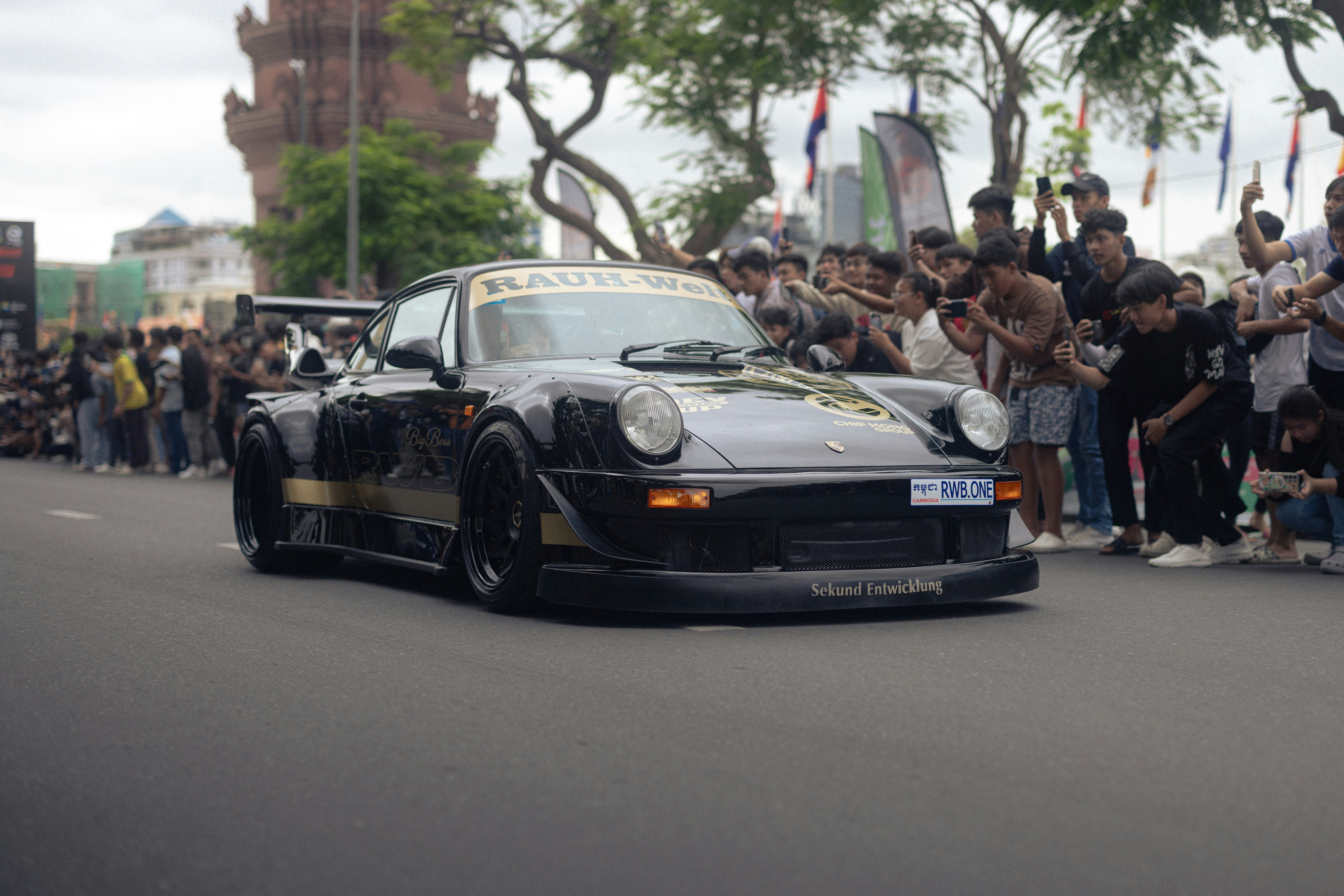 A crowd watches a custom car drive down the street.
