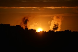 Smoke billows during a sunset over a city.