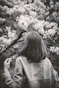 Woman gazes at blooming flowers in black and white.