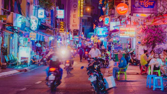 Neon-lit street with people and motorbikes at night.