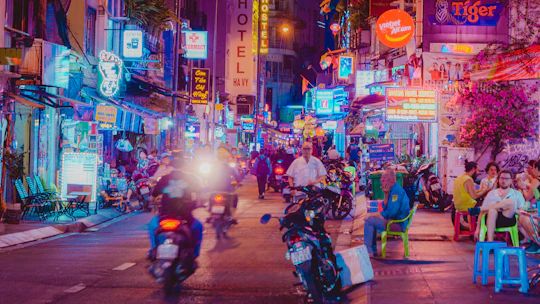 Neon-lit street with people and motorbikes at night.