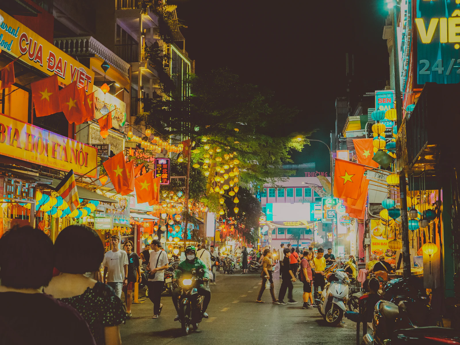 Busy night street in Ho Chi Minh City with flags, lanterns and scooters