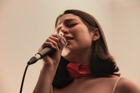 A woman sings into a microphone, eyes closed.