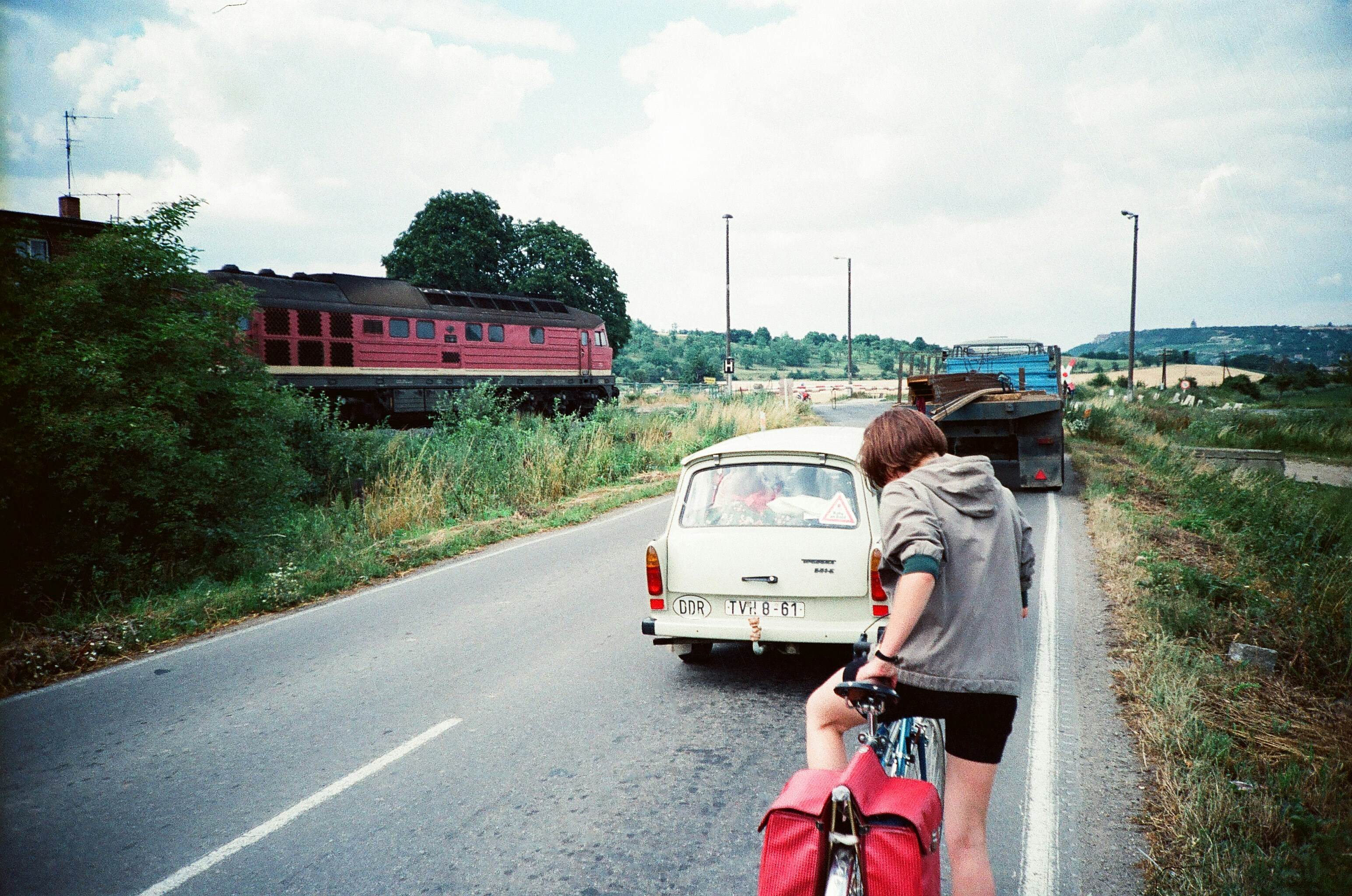 Person on bike next to car, with train in background.