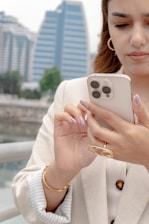 Woman uses her phone outdoors with a city backdrop.