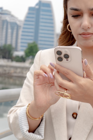 Woman uses her phone outdoors with a city backdrop.