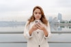 Woman looks at her phone with a city backdrop.