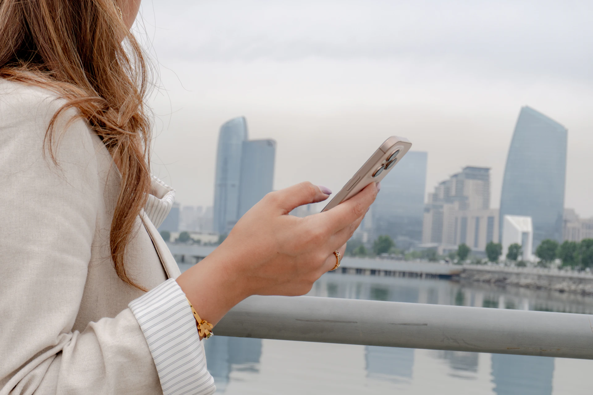 Woman checks her phone with cityscape in the background.