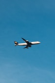 A plane flies high against a clear blue sky.