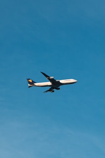 A plane flies high against a clear blue sky.