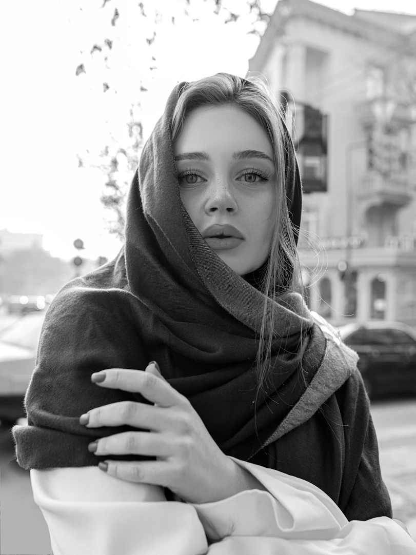 A woman poses in a scarf outdoors.