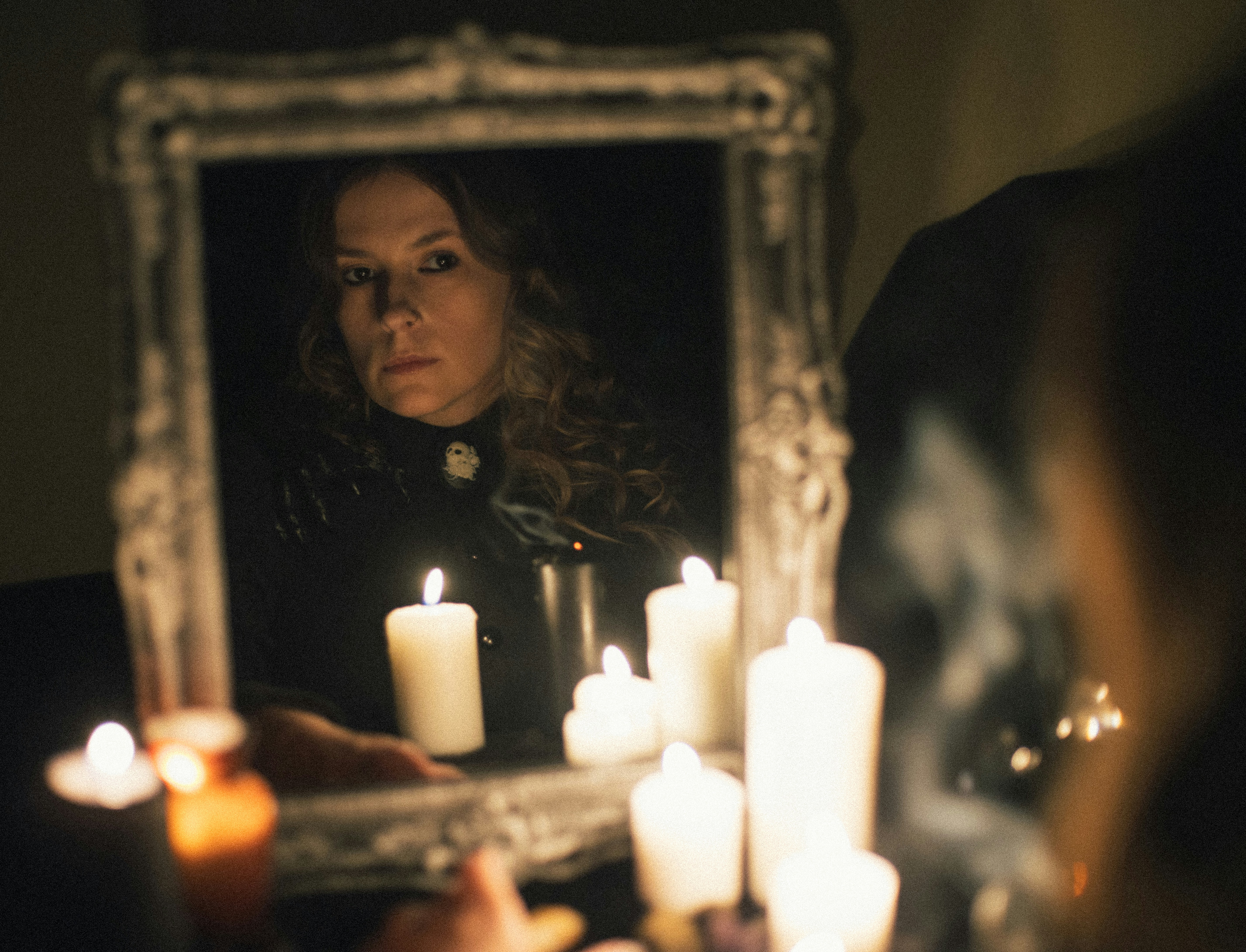 Woman gazes in a mirror lit by candlelight.