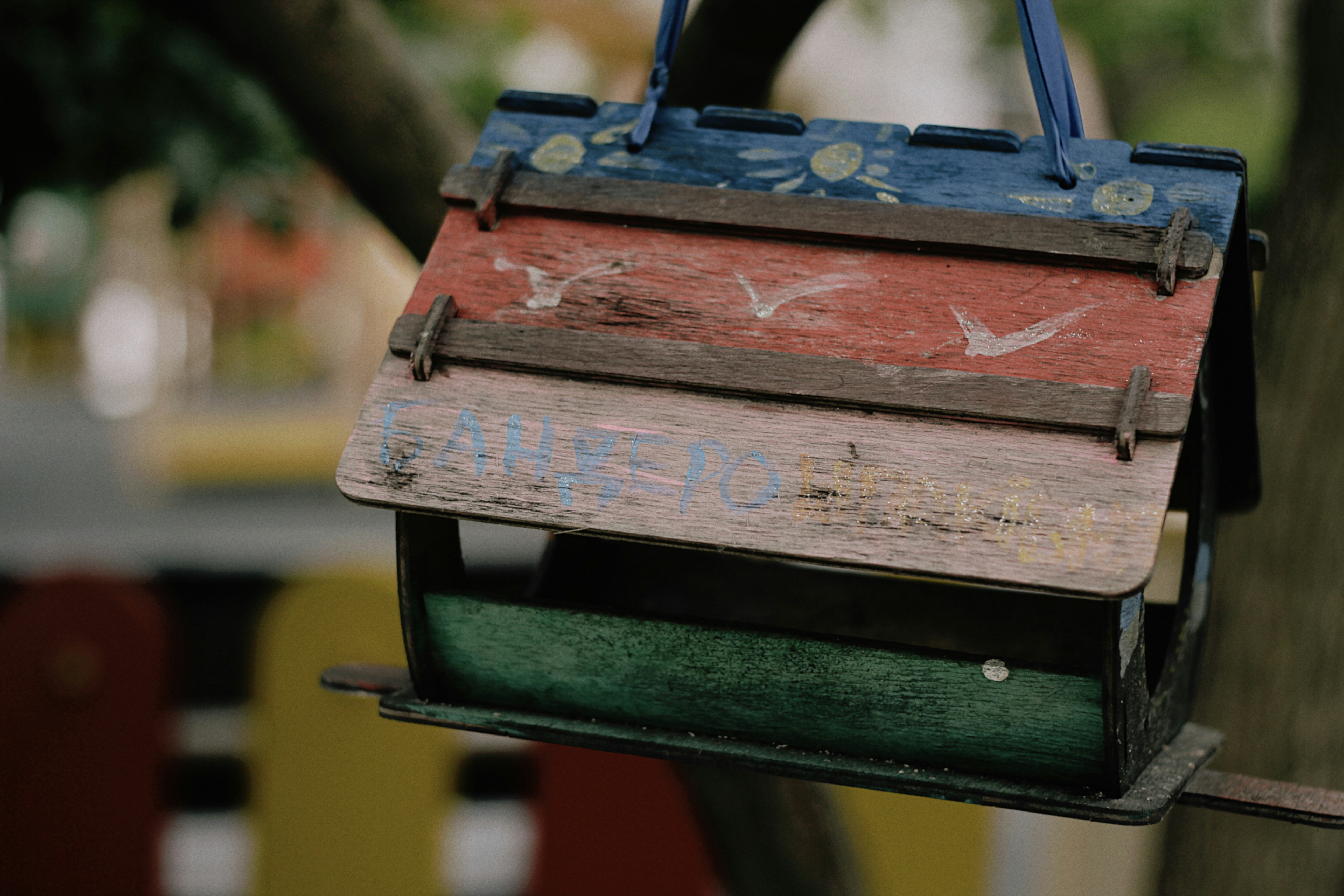 A colorful, rustic birdhouse hangs from a branch.