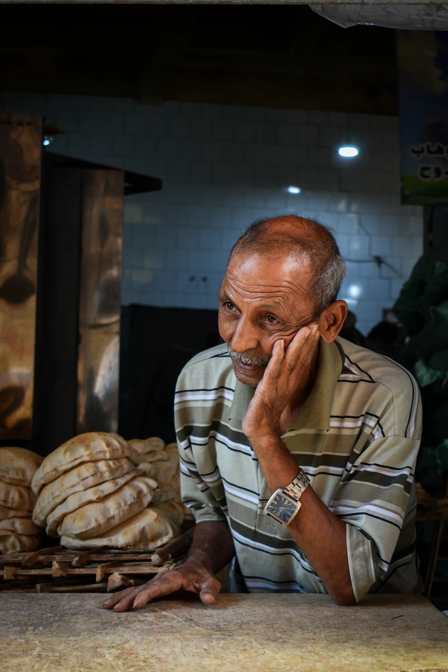 A man leaning on a bakery counter with a row of finished loaves in front of him