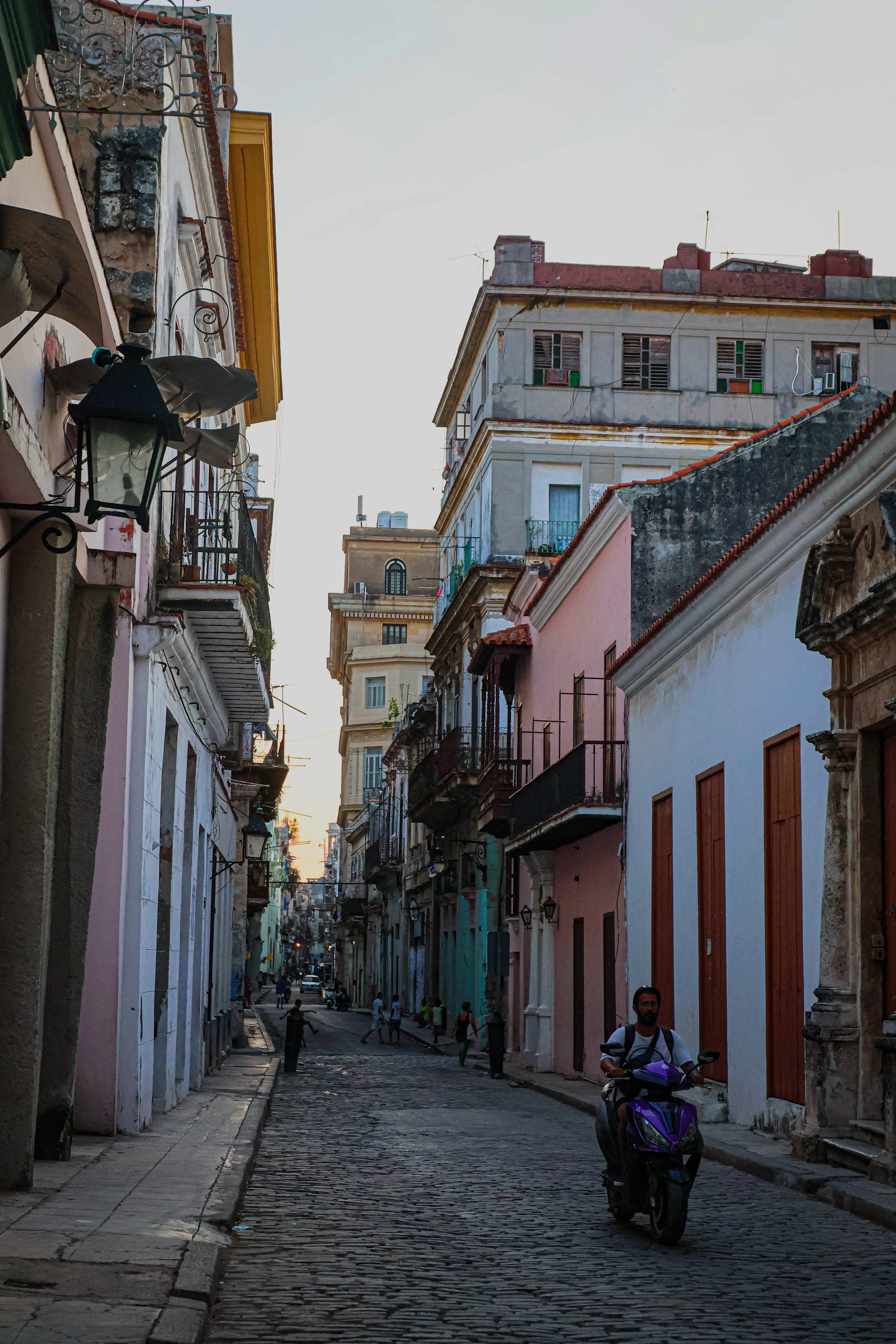 A scooter passes down a narrow cobbled street of Havana Vieja in soft dusk light.