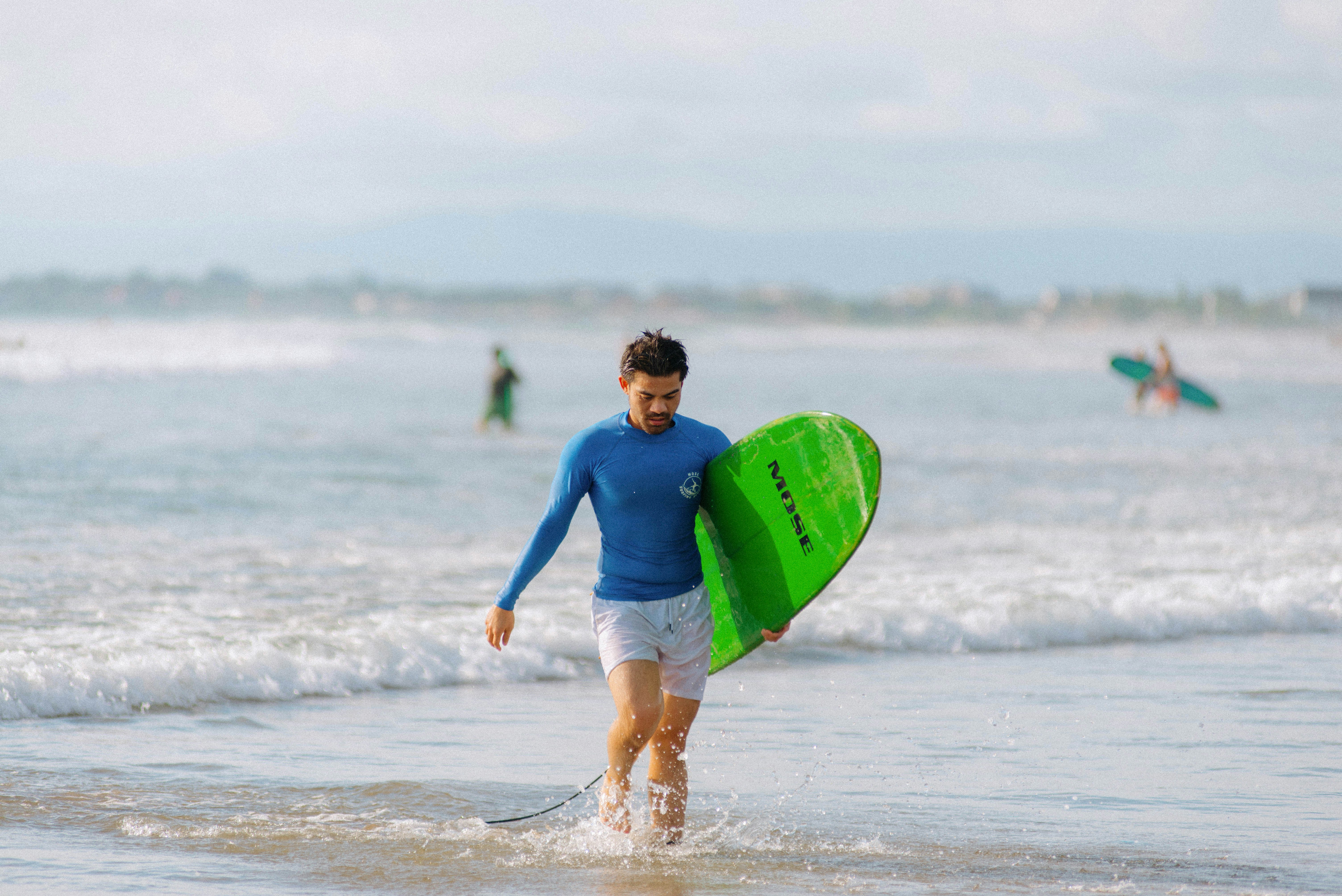 Man wades through water, holding a surfboard.